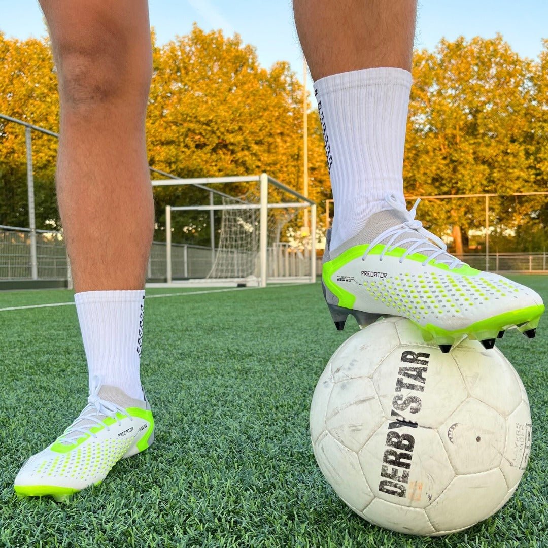 Voetballer met witte Prostec gripsokken en voetbalschoenen op bal, toont sportieve voetbalaccessoires