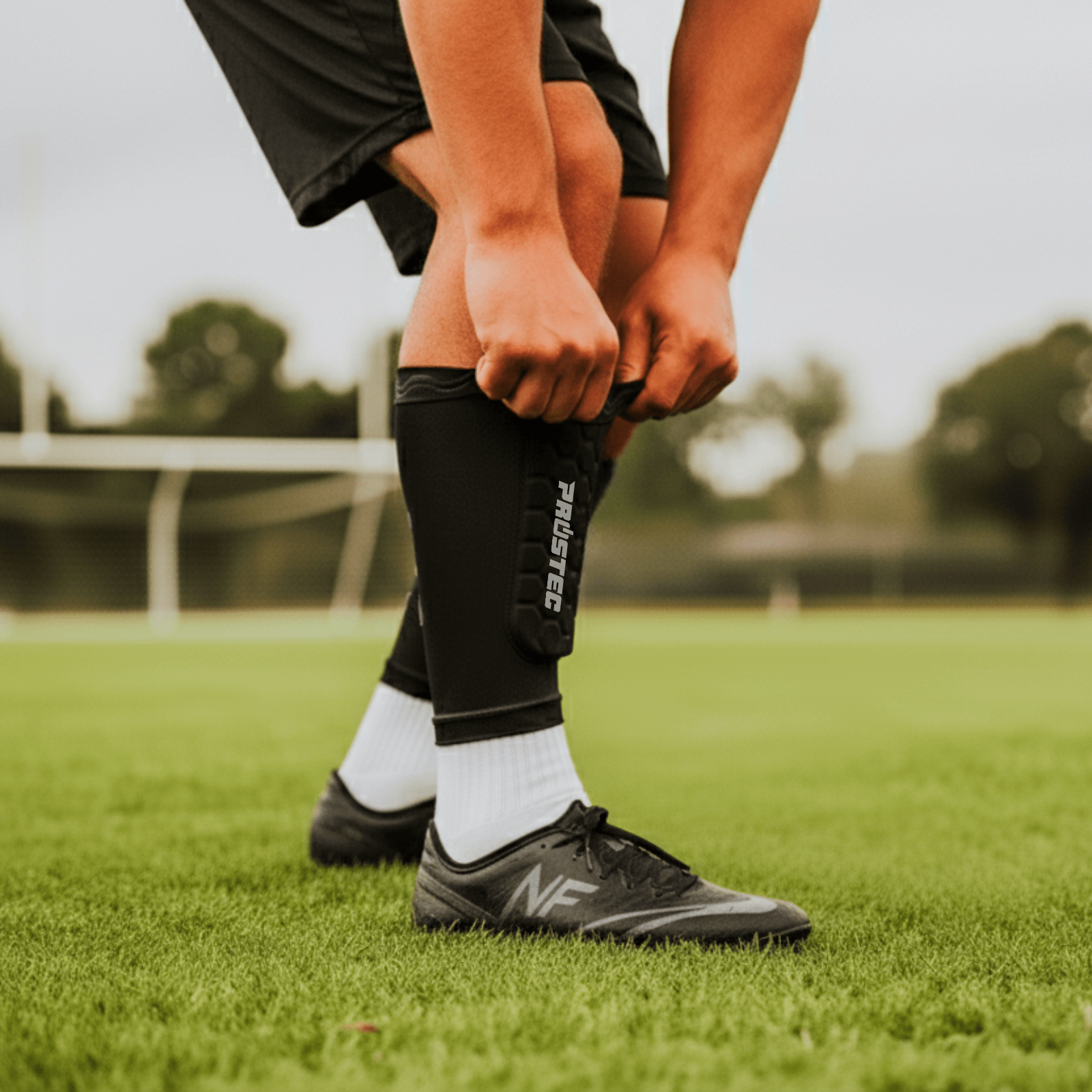 Voetballer trekt zwarte Prostec scheenbeschermer sleeve met hexagonale padding aan, cruciaal voetbalaccessoire