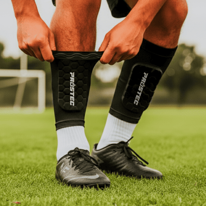 Voetballer trekt zwarte Prostec Scheenbeschermer Sleeve aan met hexagonale pads op groen voetbalveld